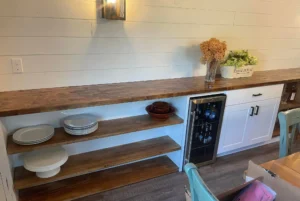 A long counter along the wall of a dining room with shelves below it, as well as a mini fridge and cabinets.